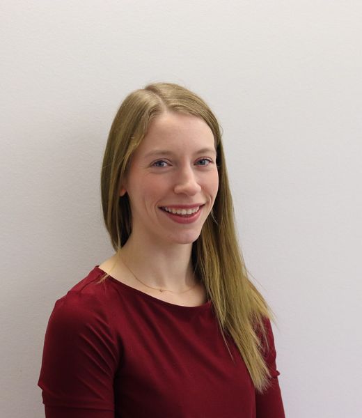 Julia Lücking lächelnd in dunkelrotem Oberteil vor heller Wand